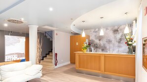Una moderna hall d'albergo con una reception, un divano bianco e una scala che conduce ai piani superiori.