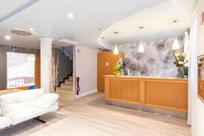 Een moderne hotelhal met een receptiebalie, een witte bank en een trap naar de andere verdiepingen.