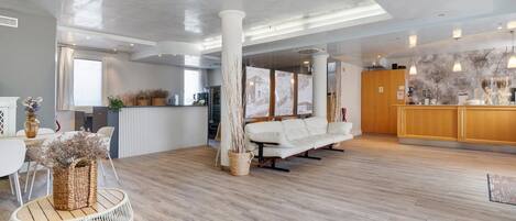 Un hall d’hôtel spacieux, doté d’un plancher en bois, d’un canapé blanc, d’un comptoir d’accueil et d’une grande fenêtre.