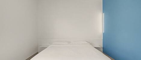 A minimalist hotel room with a single bed, a nightstand, and a blue accent wall.