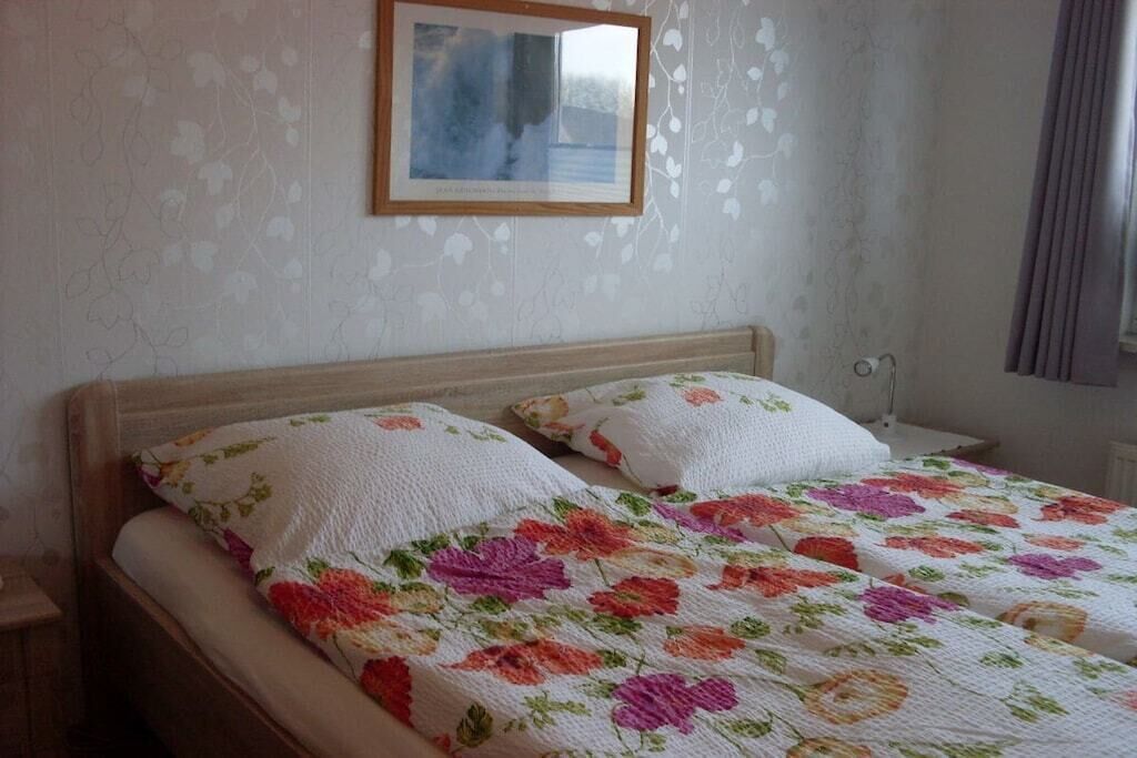 A bed with a floral quilt, a wooden headboard, and a framed picture on the wall.