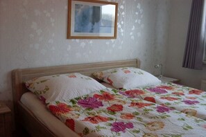 Una cama con colcha floral, cabecera de madera y un cuadro en la pared.