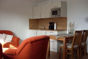 Eine kompakte Küche mit Mikrowelle, Kaffeemaschine und einem Essbereich mit Stühlen und Tisch.