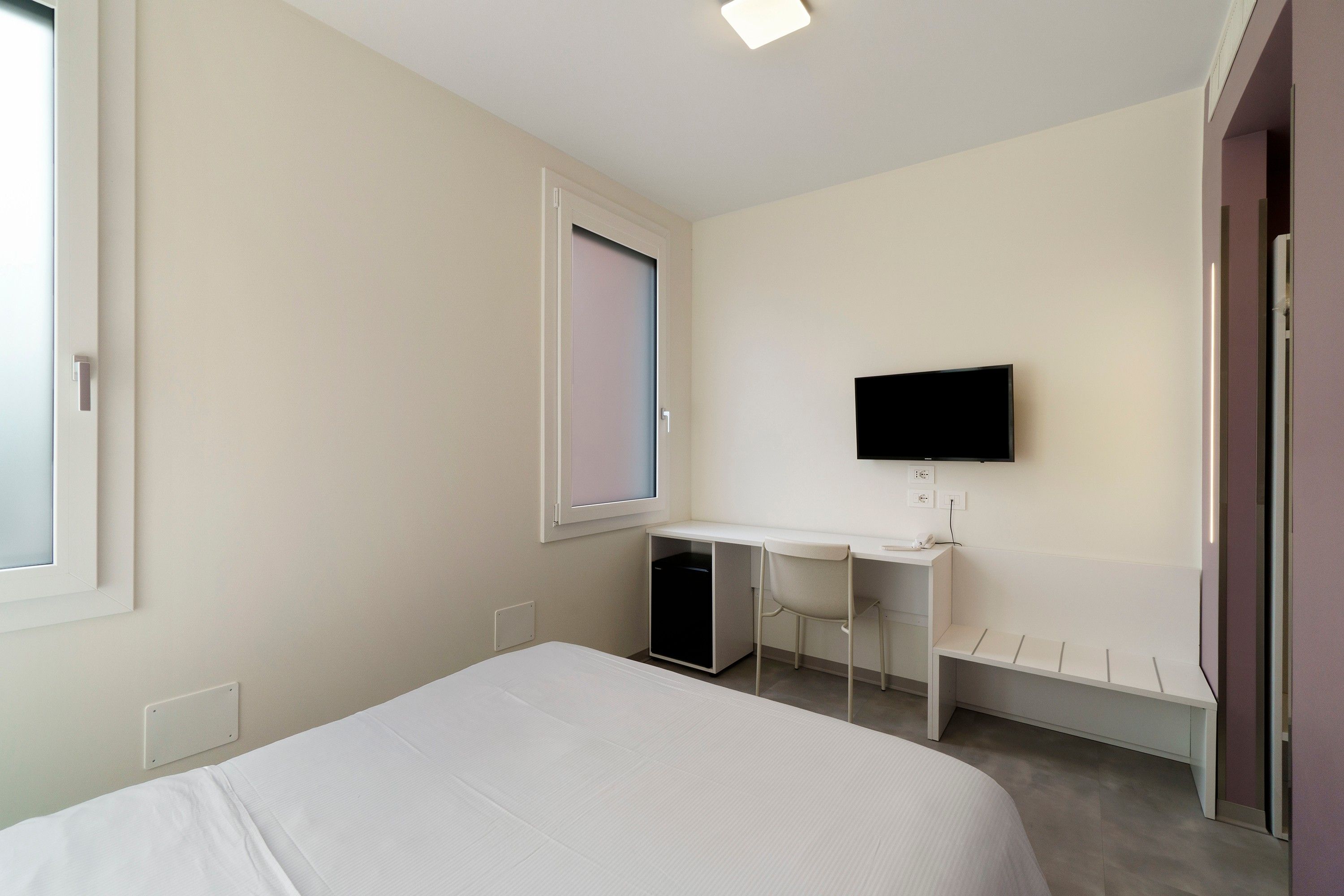Una camera da letto con un letto, una scrivania, una sedia, una televisione e una finestra.