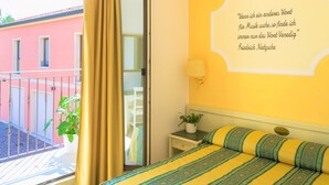 A hotel room with a bed, a bedside table with a lamp, a window with curtains, and a wall quote.