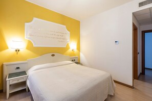 Een hotelkamer met een bed, nachtkastje, wandlamp en een deur.