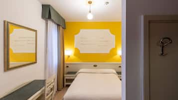 A hotel room with a bed, a desk, a chair, a nightstand, and a wall with a quote.