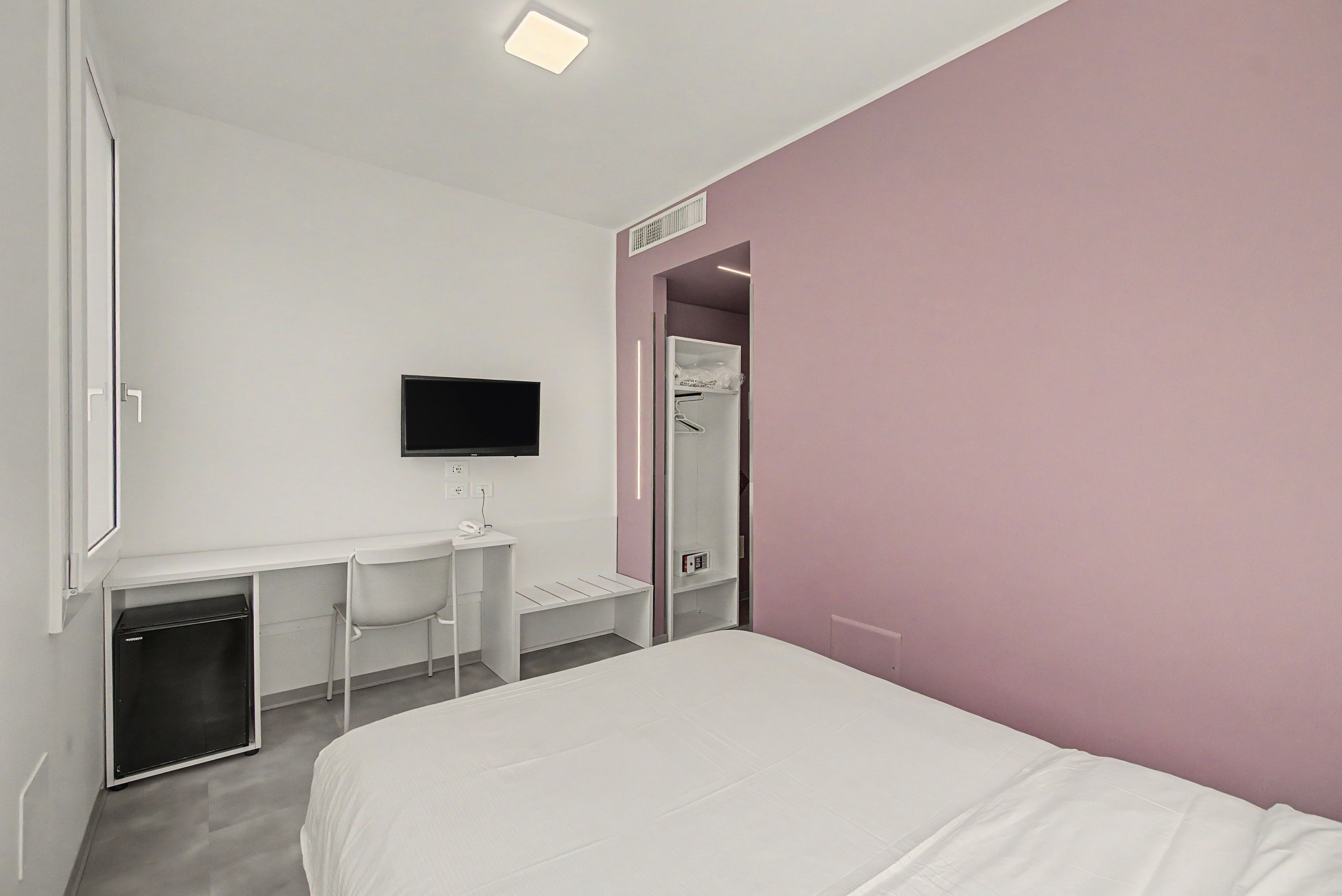 Ein Hotelzimmer mit einem Bett, einem Schreibtisch mit Stuhl, einem Fernseher und einem Kleiderschrank.