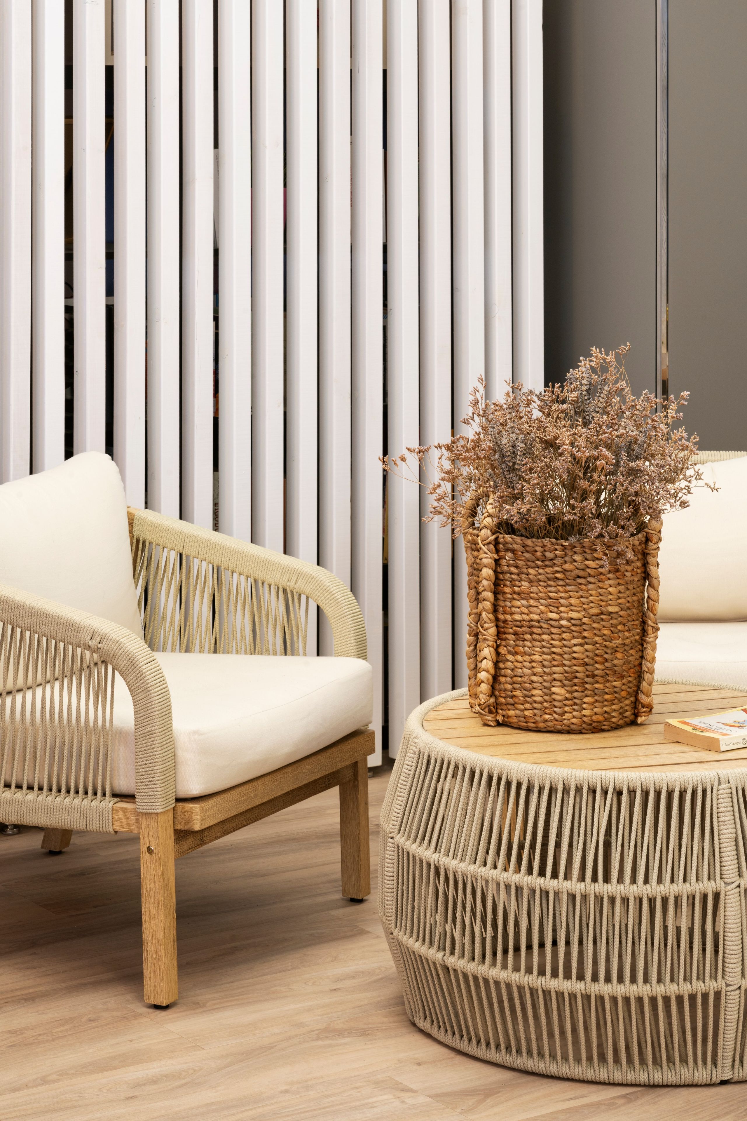 Une chaise en osier avec un coussin et un tabouret tressé sur lequel est posé un panier rempli de fleurs séchées.