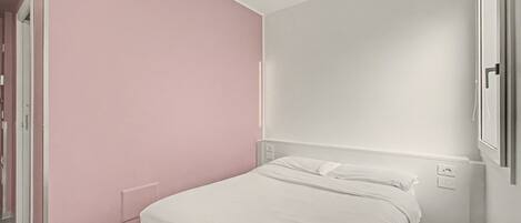 A bedroom with a single bed, a door, and a wall with a switchboard.