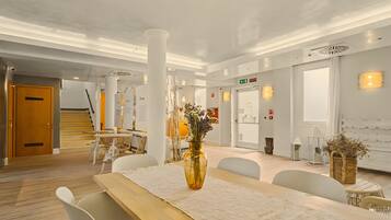En moderne hotellobby med en træreception, hvide stole, en stor vase med blomster og en trappe til et andet område.