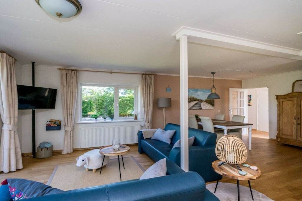 A living room with a sofa, a television, a dining table, and a window with curtains.