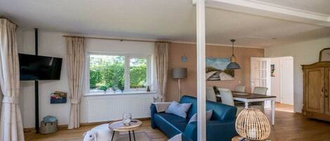 A living room with a sofa, a television, a dining table, and a window with curtains.