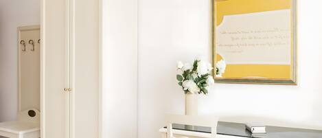 A room with a white wardrobe, a desk with a vase of flowers, and a framed quote on the wall.