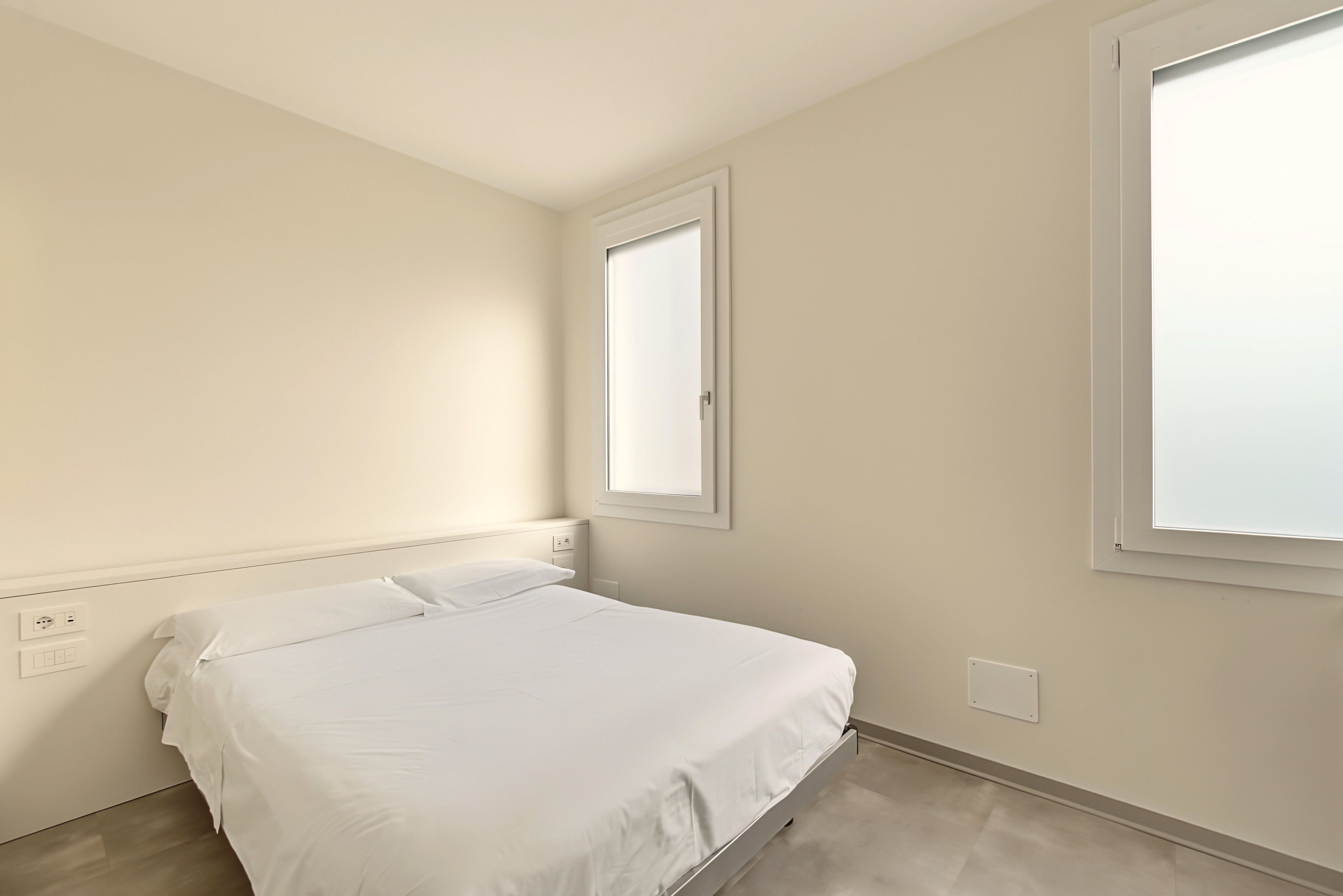 A bedroom with a single bed, a window, and a wall socket.