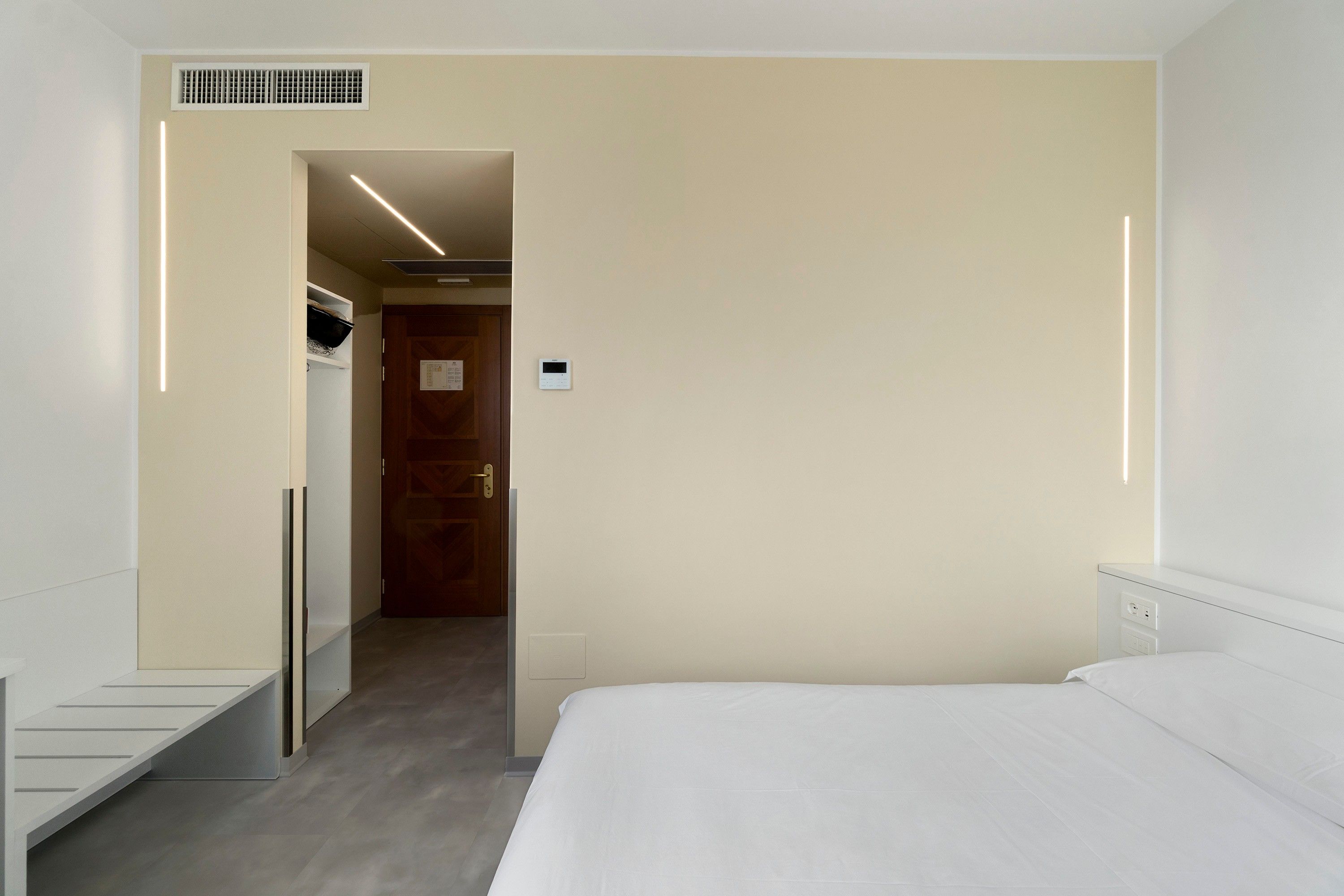 Une chambre d’hôtel équipée d’un lit, d’une armoire, d’une porte et d’un thermostat fixé au mur.