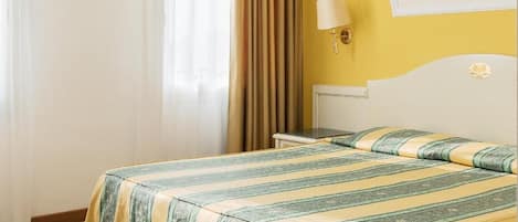 A hotel room with a bed, curtains, a nightstand, and a wall-mounted lamp.