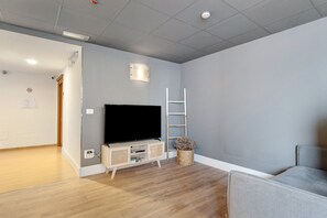Una habitación con una televisión de pantalla plana sobre un soporte de madera, una escalera blanca y una cesta tejida con flores secas.