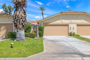 A residential property with a garage, a palm tree, and a well-maintained lawn. - Monterey Country Club Condo | Golf Course & Lake Views, Gated Community, Heated Pools, Palm Desert (Palm Desert)