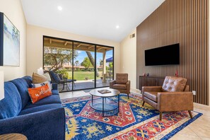 A living room with a blue sofa, a coffee table, and two leather armchairs. A flat-screen TV is mounted on the wall. - Monterey Country Club Condo | Golf Course & Lake Views, Gated Community, Heated Pools, Palm Desert (Palm Desert)
