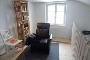 A room with a black leather chair, a white chair, a bookshelf, and a window. - Holiday home in Monschau with swimming pool (Monschau)