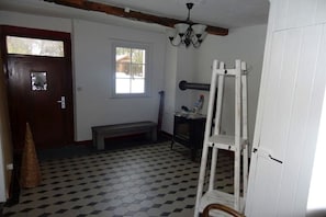 Una stanza con pavimento a scacchi, una porta in legno, una panca, un cavalletto bianco e una finestra.