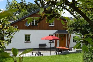 A two-story house with a wooden exterior and white walls, a patio with a table and chairs, and a red umbrella. - Holiday home in Monschau with swimming pool (Monschau)