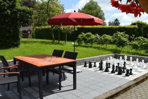 Ein Schachspiel im Freien auf befestigtem Untergrund, mit einem Tisch und Stühlen in der Nähe.