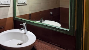 A bathroom with a white sink, a green-framed mirror, and a shower head. - Hasu Stay (coorg)