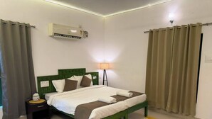 A hotel room with a bed, a bedside table, an air conditioning unit, a lamp, and curtains. - Hasu Stay (coorg)