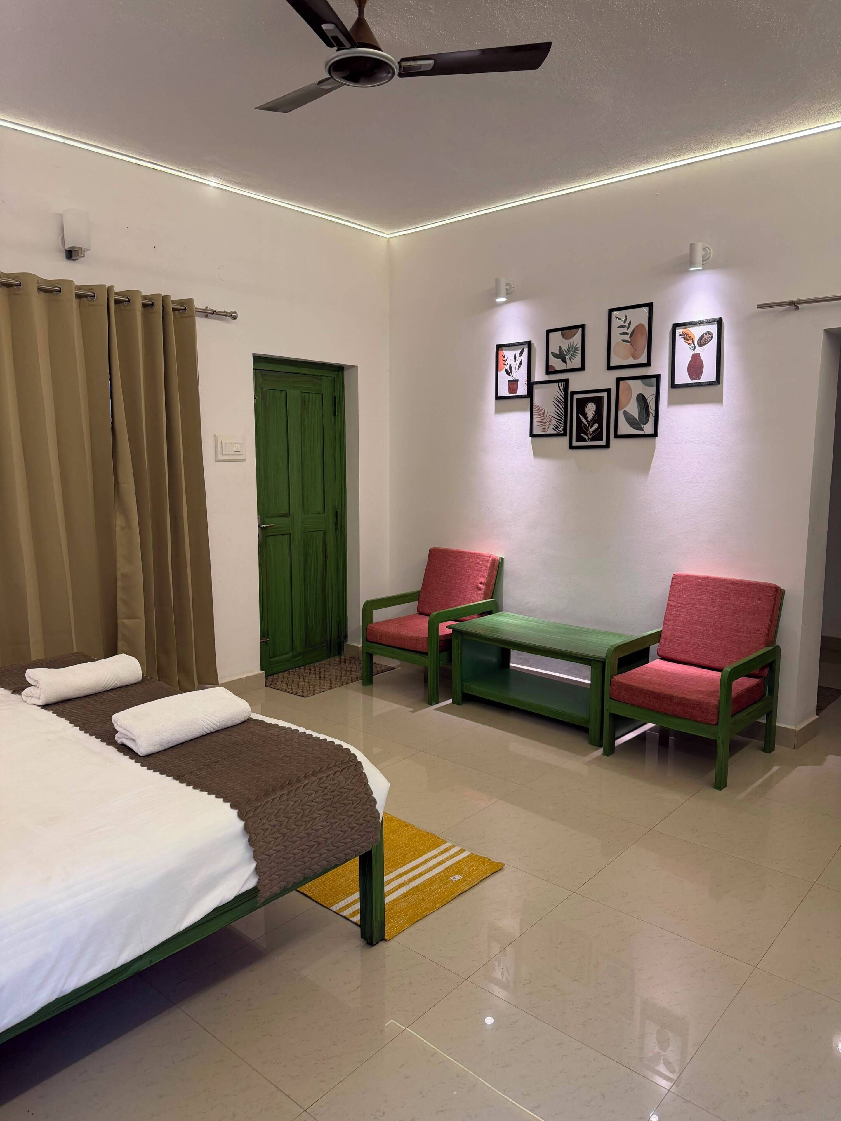 Habitación de hotel con cama, dos sillas, una puerta verde y obras de arte colgadas en la pared.