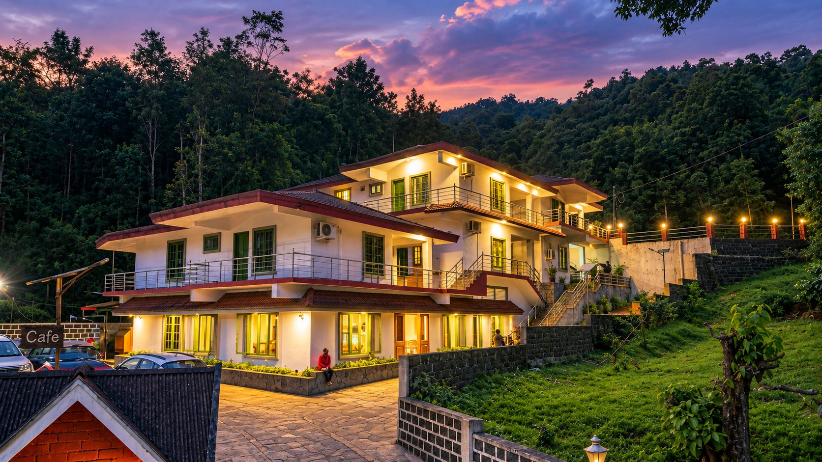 Un hotel de varios pisos con balcón, un letrero de cafetería y una pared de piedra.
