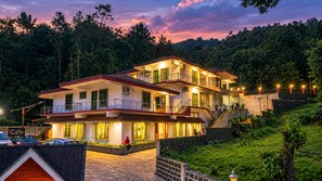A multi-story hotel with a balcony, a cafe sign, and a stone wall. - Hasu Stay (Madikeri)