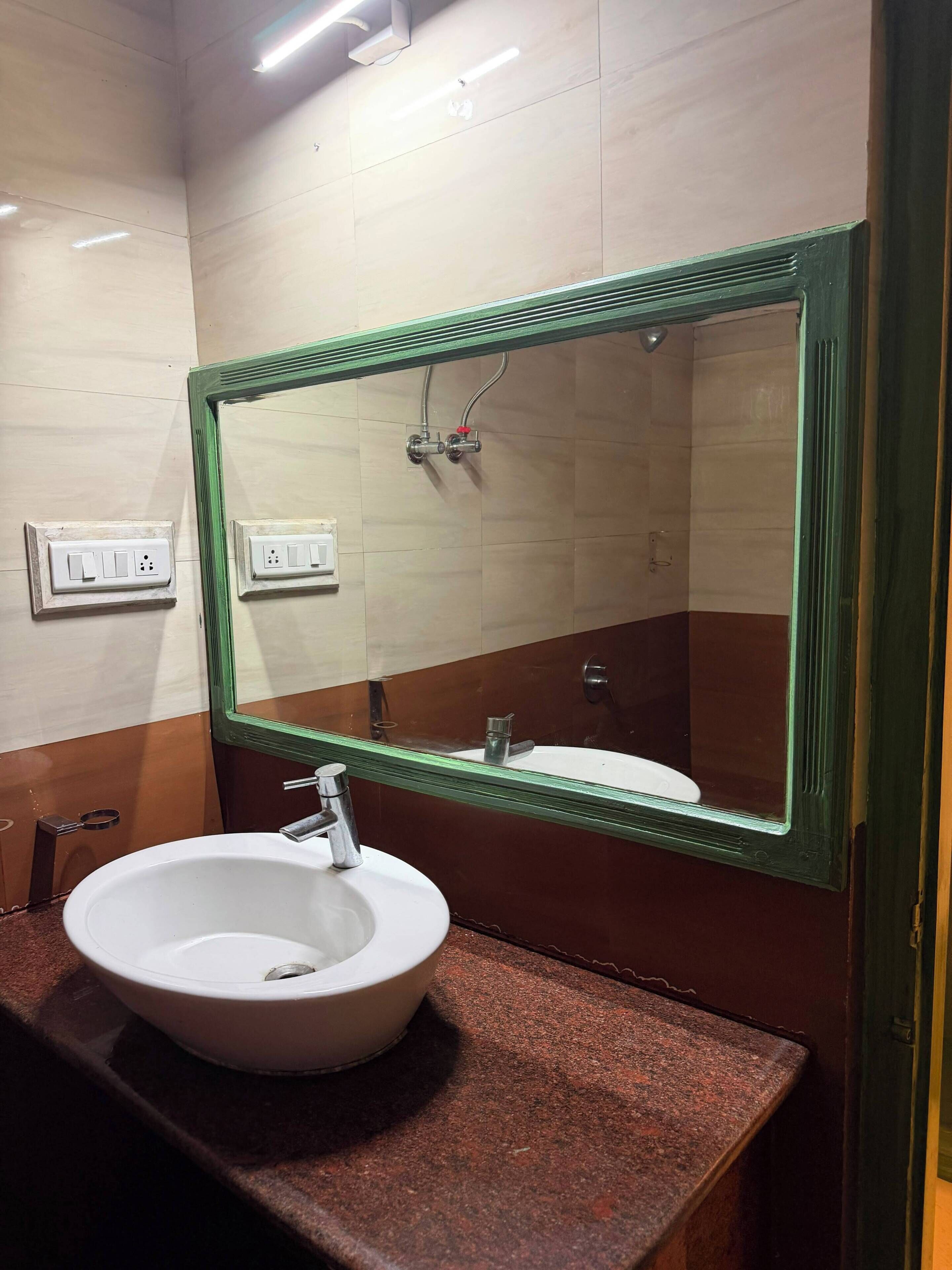 Un baño con un lavamanos blanco, un espejo con marco verde y un cabezal de ducha.