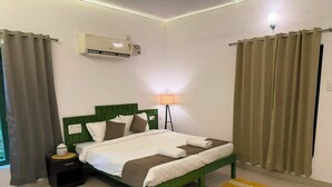 A neatly made bed with a green headboard, a bedside lamp, and a small nightstand. - Hasu Stay (coorg)