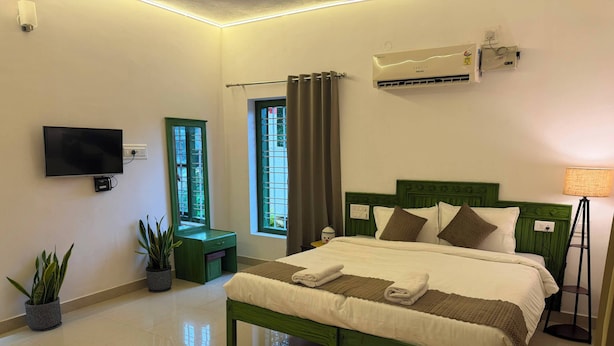 A hotel room with a bed, a television, a window, and an air conditioning unit. - Hasu Stay (coorg)