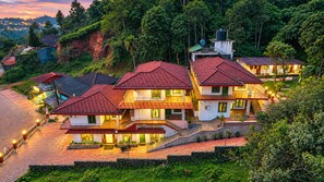 Un hôtel à plusieurs étages, doté d’un toit recouvert de tuiles rouges, d’une piscine et offrant une vue sur le paysage environnant.