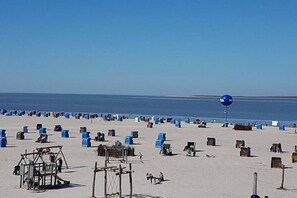 Een strand met tal van blauwe en bruine strandstoelen en parasols, een houten constructie, en een heldere lucht.