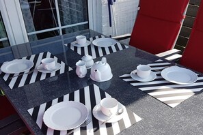 Een tafel gedekt voor vier personen, met geribbelde placemats, witte borden, bekers en een theepot.