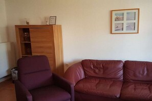 Ein Wohnzimmer mit einem braunen Ledersofa, einem violetten Sessel und einer Holzkabine mit Gläsern.