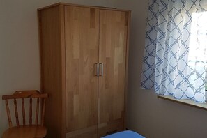 Een kamer met een houten garderobe, een houten stoel en een raam met gordijnen met een patroon.