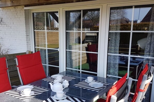 Een eethoek met een tafel voor vier personen, stoelen met rode kussens, en een glazen scheiding.