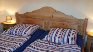 Cama de casal com roupa de cama listrada, cabeceira de madeira e abajures.