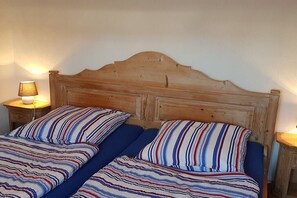 Een tweepersoonsbed met gestreept beddengoed, een houten hoofdbord en nachtlampjes.