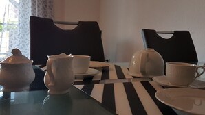 Uma mesa de jantar com toalha listrada em preto e branco, dois bules, duas xícaras e uma tampa de bule.
