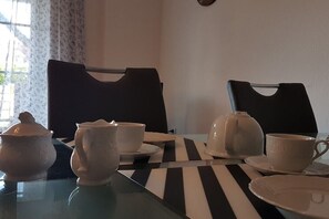 Een eettafel met een zwart-wit gestreepte tafelkleed, twee theepotten, twee kopjes en een theepotdeksel.