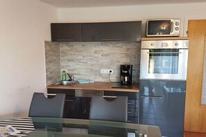 Een compacte keuken met een magnetron, oven en koffiezetapparaat. Er is een eettafel met stoelen.