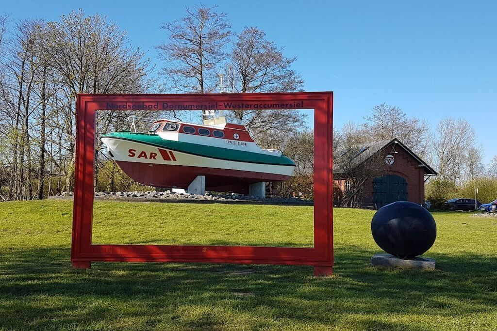 Ein gerahmtes Modellboot mit dem Schriftzug 'Nordsøbad Dornumersiel - Westeraccummsiel' und ein kleines Gebäude mit einer Uhr.