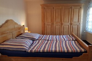 Een enkel bed met houten hoofdbord en gestreept beddengoed, een houten kledingkast en een raam met uitzicht.