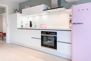 Eine moderne Küche mit weißen Schränken, einem eingebauten Ofen und einem pinken Kühlschrank.
